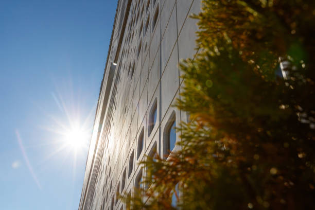 Low angle view from city street on corporate building exterior, concrete block wall and uneven windows, sunny sky, lens flare