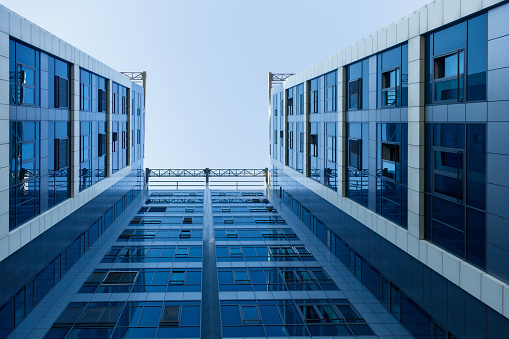 Low angle view on blue glass and concrete corporate building facade towards clear sky, directly below