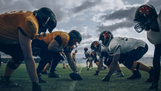 zwei professionelle american football-teams stehen sich gegenüber und sind bereit, das spiel zu beginnen. verteidigung und offensive bereiten sich darauf vor, um den ball zu kämpfen, mit dem wunsch, punkte zu erzielen und das tor zu erzielen und zu gewin - sport university football player action stock-fotos und bilder