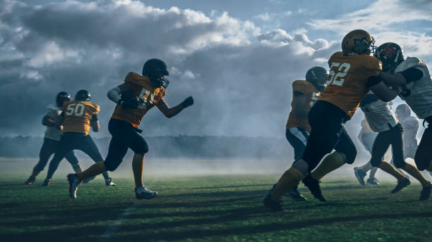 campo de futebol americano duas equipes jogam: jogador bem sucedido correndo em torno de jogadores de defesa para marcar pontos de touchdown. atletas profissionais competem pela bola, lutam pela vitória. - football player group of people running american football - fotografias e filmes do acervo