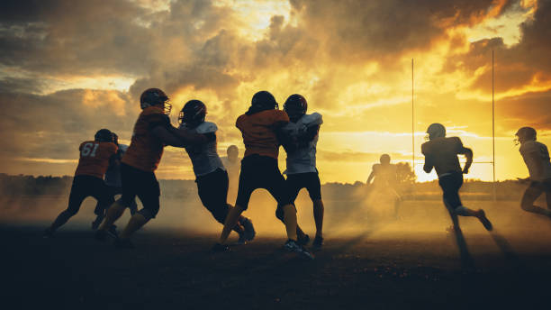 campo de fútbol americano dos equipos compiten: los jugadores pasan y corren atacando para anotar puntos de touchdown. los atletas profesionales luchan por la pelota, el tackle. puesta de sol de la hora dorada - pass the ball fotografías e imágenes de stock