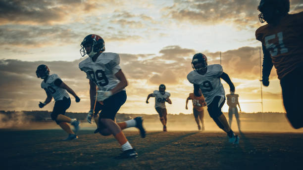 campo de fútbol americano dos equipos compiten: los jugadores pasan y corren atacando para anotar puntos de touchdown. los atletas profesionales luchan por la pelota, el tackle. toma de la puesta de sol de la hora dorada - pass the ball fotografías e imágenes de stock