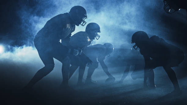 american football field zwei teams treten gegeneinander an: spieler passen, laufen, greifen an, um touchdown-punkte zu erzielen. regnernacht mit athleten kämpfen in dramatischem rauch um den ball. - football player american football athlete sport stock-fotos und bilder