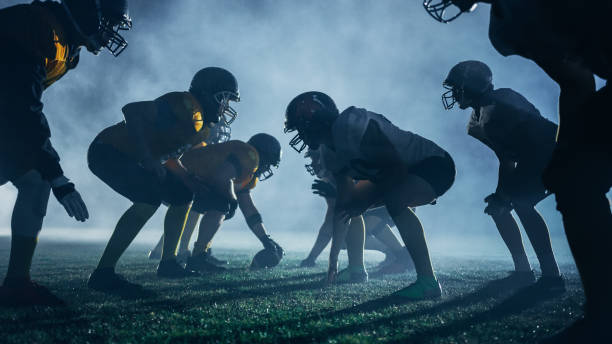 campo de fútbol americano dos equipos se paran uno frente al otro, listos para comenzar el juego. atletas profesionales listos para competir por la pelota y luchar por la victoria. dramática niebla nocturna azul - american football playing touchdown team sport fotografías e imágenes de stock