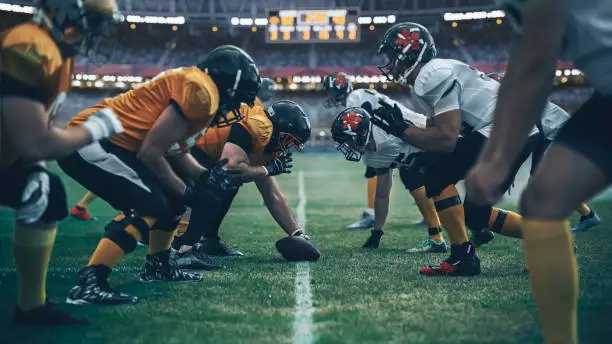 Photo of American Football Championship. Teams Ready: Professional Players, Aggressive Face-off, Ready for Pushing, Tackling. Competition Full of Brutal Energy, Power. Stadium Shot with Dramatic Light