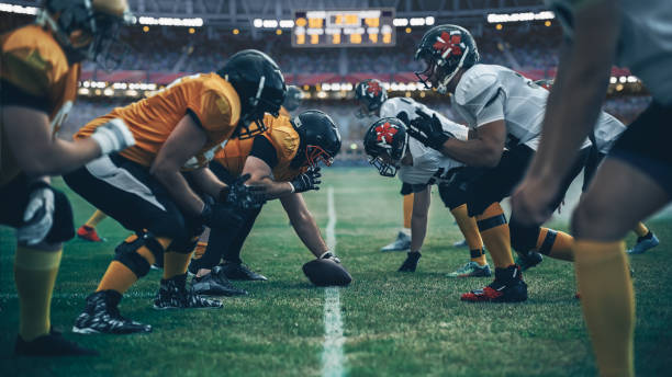 american football championship. teams ready: professional players, aggressive face-off, ready for pushing, tackling. competition full of brutal energy, power. stadium shot with dramatic light - bola de futebol imagens e fotografias de stock