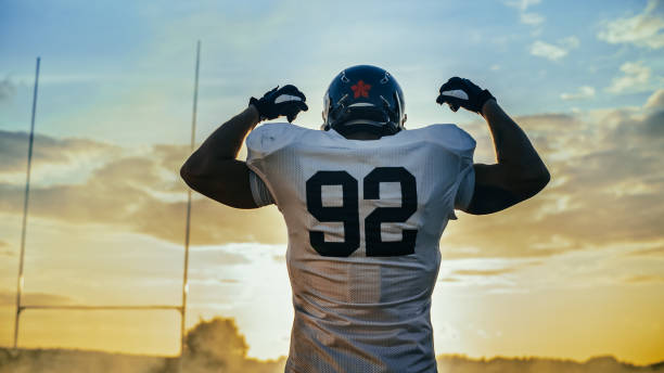 American Football Championship Game: Powerful Player Wearing Helmet, Flexing His Muscles Dramatically. Professional Athlete Determined to Win. Cheerful Sportsman Celebrating. Back View Shot American Football Championship Game: Powerful Player Wearing Helmet, Flexing His Muscles Dramatically. Professional Athlete Determined to Win. Cheerful Sportsman Celebrating. Back View Shot american football player stock pictures, royalty-free photos & images