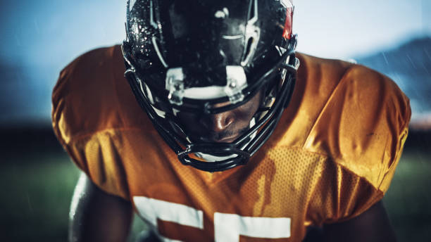 football américain: gros plan d’un joueur afro-américain professionnel regardant la caméra. athlète héros prêt à remporter le championnat. détermination, compétence, puissance. portrait dramatique - football helmet playing field american football sport photos et images de collection