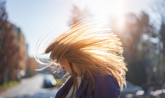Portrait of a young happy woman in the city in the sunny rays with flying hair