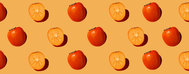 istock Autumn pattern is made with half a persimmon on a orange background. 1355089444