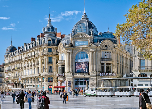 Montpellier, France - October 27, 2021: View of the Place de la Comédie with a cinema, pedestrians and a tourist train in Montpellier, France.