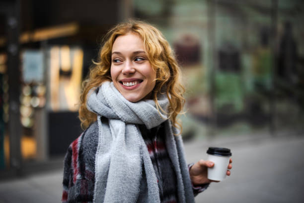 jeune femme avec tasse de café souriante à l’extérieur - ville milieu urbain photos et images de collection