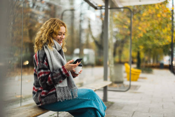 istock Young woman using smart phone at bus station 1355091291