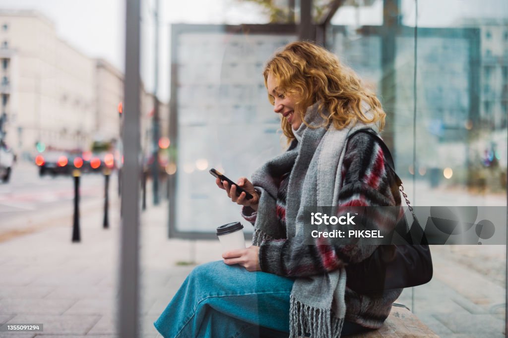 Young woman using smart phone at bus station Bus Stop Stock Photo