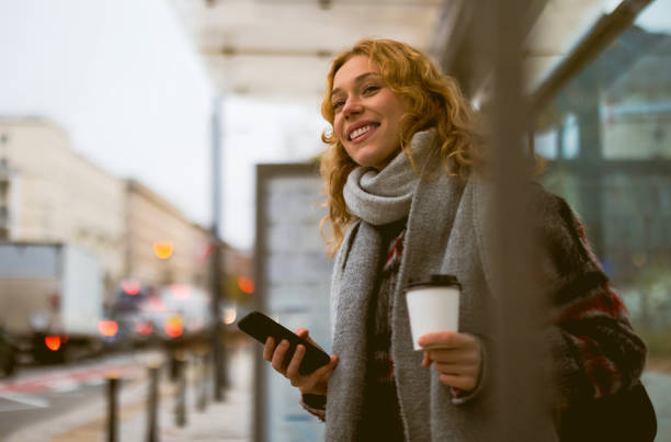 istock Young woman using smart phone at bus station 1355091369