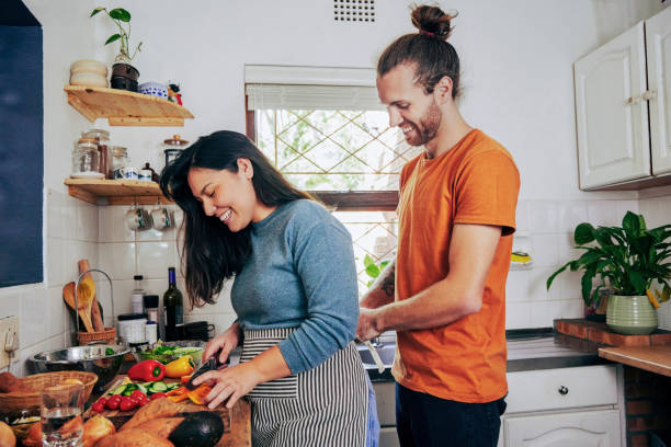 istock Shot of a young man tying on his wife's apron while she chops vegetables 1355092591