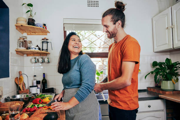 Shot of a young man tying on his wife's apron while she chops vegetables