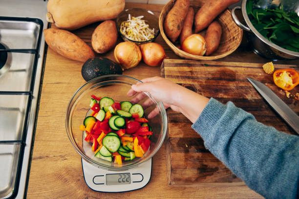 foto de una mujer joven pesando un tazón de verduras - instrument of weight fotografías e imágenes de stock