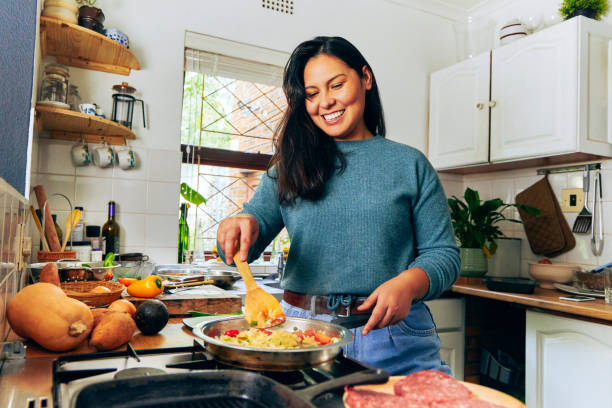 снимок молодой женщины, помешивающей овощи на плите - patty pan стоковые фото и изображения