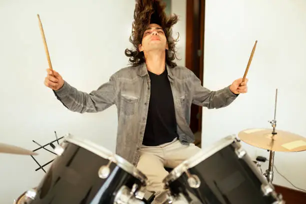 Young man rocking out on a set of drums inside of a home recording studio during a band rehearsal session