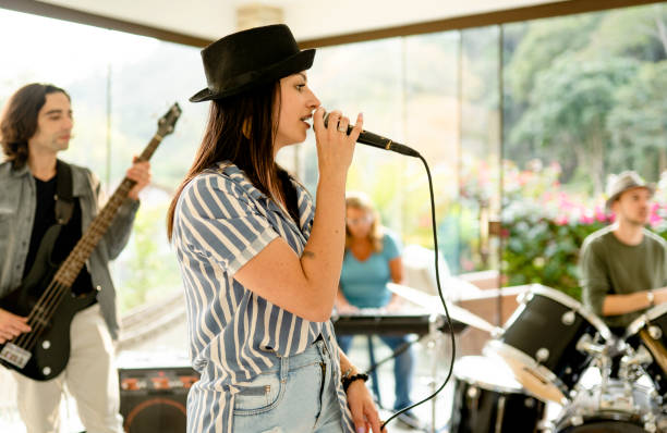 istock Young woman singing into a mic during a band rehearsal session 1355093031