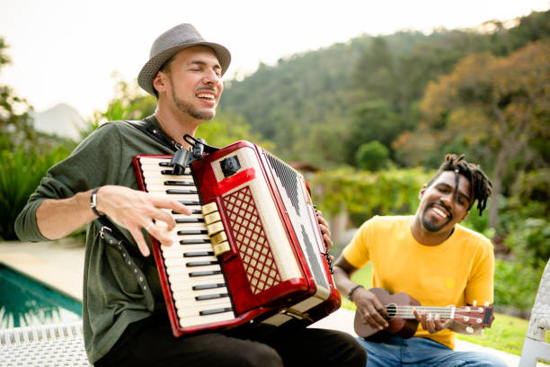 Two diverse young musicians jamming with different instruments outside Two diverse young musicians smiling while jamming outside together with an accordion and a ukulele accordion instrument stock pictures, royalty-free photos & images