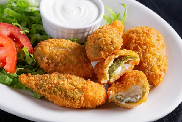 Close-up of jalapeno poppers with sour cream on a white plate