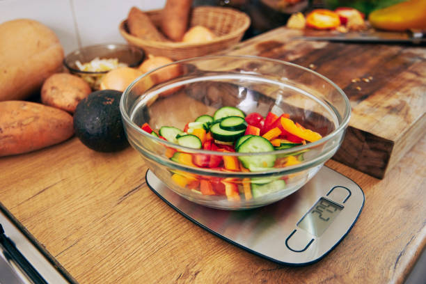 Shot of a bowl of veggies waiting to be weighed on a kitchen scale A necessary cooking instrument kitchen scale stock pictures, royalty-free photos & images