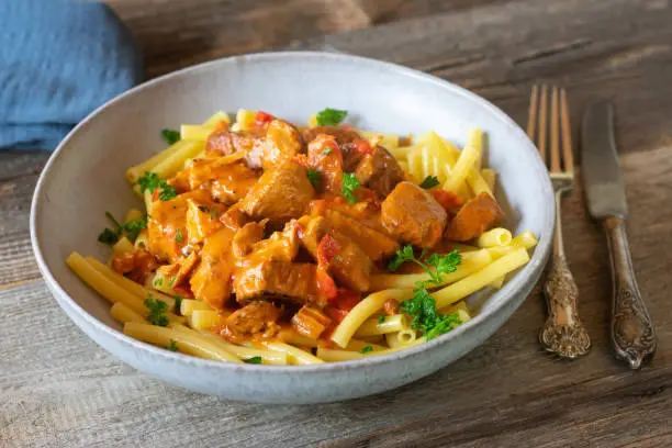 Homemade fresh cooked goulash, stew or ragout with cubed turkey breast and macaroni in a delicious paprika sauce. Served on a plate isolated on wooden table