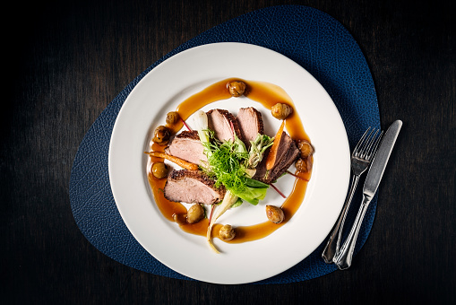Plate of Berberi duck breast served with roasted seasonal vegetables, chestnuts and a duck infused sauce. Colour, overhead view, horizontal format with some copy space. Shot on location at a restaurant on the island of Moen in Denmark.