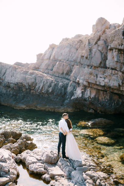 istock Groom hugs bride while standing on the stones. Back view 1355099641