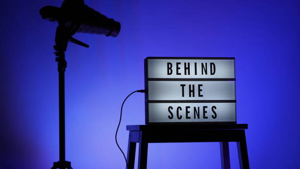 istock Behind the scenes text on Lightbox or Cinema Light box. Movie board light box on studio stair and light Snoot tripod on colors gradiant Background. Represent behind the scenes team is working on. 1355103984