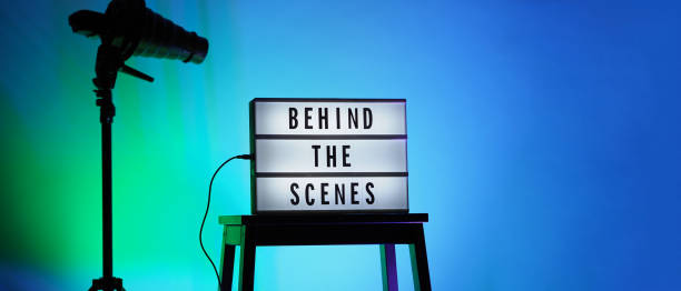 istock Behind the scenes text on Lightbox or Cinema Light box. Movie board light box on studio stair and light Snoot tripod on colors gradiant Background. Represent behind the scenes team is working on. 1355104089