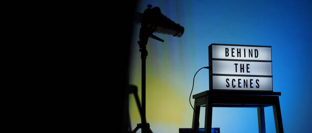 istock Behind the scenes text on Lightbox or Cinema Light box. Movie board light box on studio stair and light Snoot tripod on colors gradiant Background. Represent behind the scenes team is working on. 1355104953