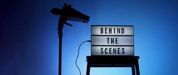 istock Behind the scenes text on Lightbox or Cinema Light box. Movie board light box on studio stair and light Snoot tripod on colors gradiant Background. Represent behind the scenes team is working on. 1355104978