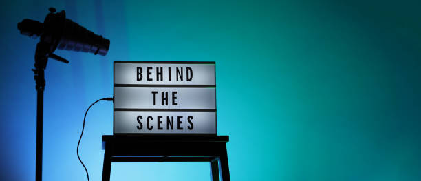 istock Behind the scenes text on Lightbox or Cinema Light box. Movie board light box on studio stair and light Snoot tripod on colors gradiant Background. Represent behind the scenes team is working on. 1355104982