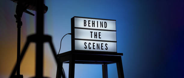 istock Behind the scenes text on Lightbox or Cinema Light box. Movie board light box on studio stair and light Snoot tripod on colors gradiant Background. Represent behind the scenes team is working on. 1355105642