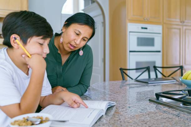Native American mom helping son with homework A Native American boy in Middle School sits at the kitchen counter and works on homework with his mom's assistance. american tribal culture stock pictures, royalty-free photos & images