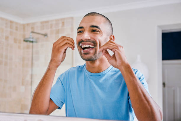 снимок молодого человека, зубной нитью в ванной комнате дома - flos стоковые фото и изображения