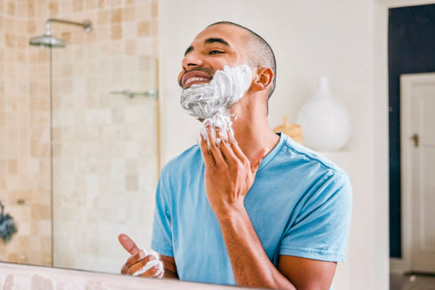 Shot of a young man applying shaving cream to his face in a bathroom at home This is calming shaving stock pictures, royalty-free photos & images