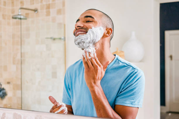 zdjęcie młodego mężczyzny nakładającego krem do golenia na twarz w łazience w domu - men shaving human face bathroom zdjęcia i obrazy z banku zdjęć