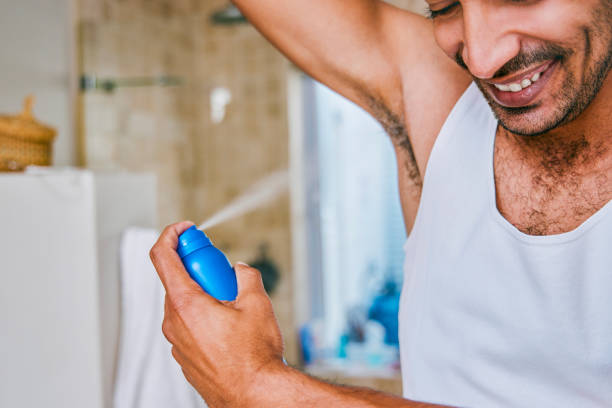 tiro de um jovem pulverizando desodorante em sua axila no banheiro de casa - deodorizing - fotografias e filmes do acervo