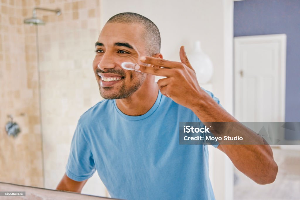 Shot of a young man applying moisturizer to his face in the bathroom at home You don't need too much Suntan Lotion Stock Photo