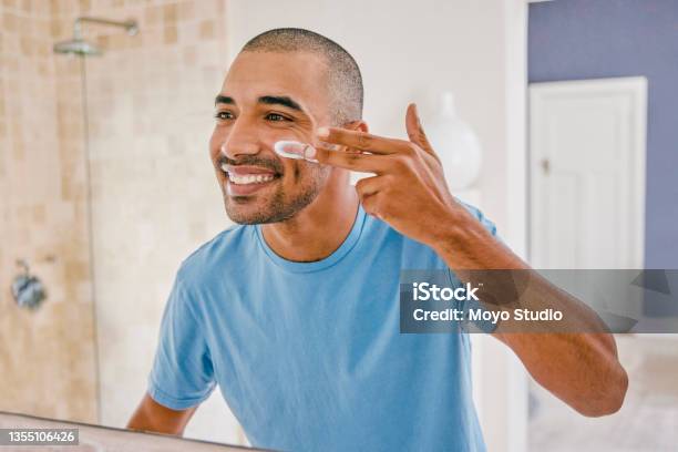 Shot Of A Young Man Applying Moisturizer To His Face In The Bathroom At Home Stock Photo - Download Image Now