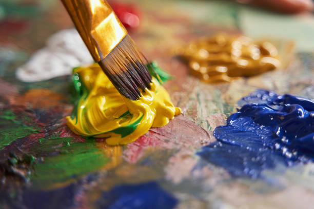 istock Painter mixing yellow and green paints with brush 1355107029