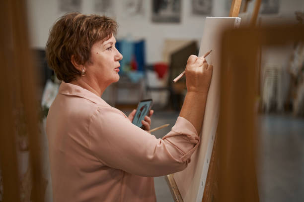 Portrait of cute female that drawing sketch Profile photo of aged woman holding telephone while copying picture painted image paintings oil paint senior women stock pictures, royalty-free photos & images