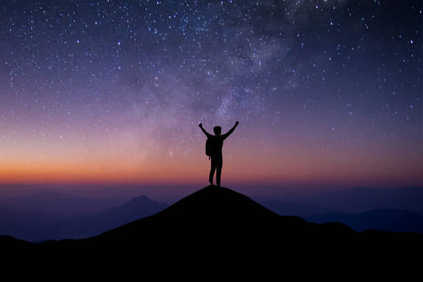 istock Young traveler with backpack standing and open both arm and watched night sky view, star and milky way alone on top of the mountain. He enjoyed traveling and was successful when he reached the summit. 1355108593