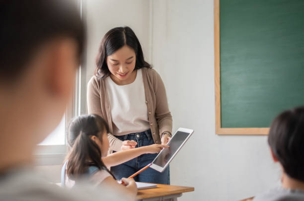 教室でデジタルタブレットで学ぶアジアの女の子を教えるアジアの美しい女性教師 - 小学生 ストックフォトと画像