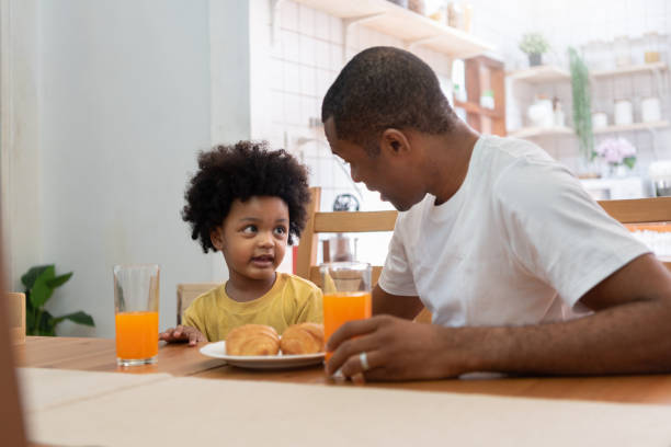 padre afroamericano hablando con su hijo en la mesa del comedor - domestic kitchen father eating child fotografías e imágenes de stock