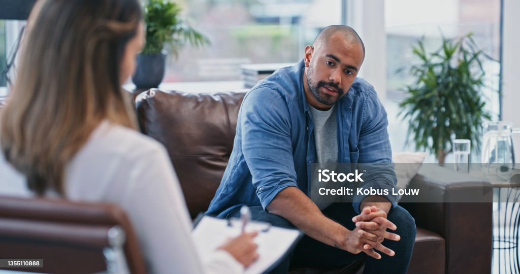 Cropped shot of a handsome young man looking thoughtful while sitting in session with his female therapist Where do I begin? Psychotherapy Stock Photo